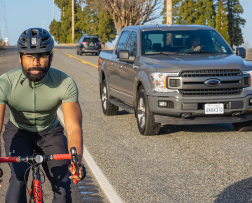 Image of a biker cycling on the road with a truck safely passing them.